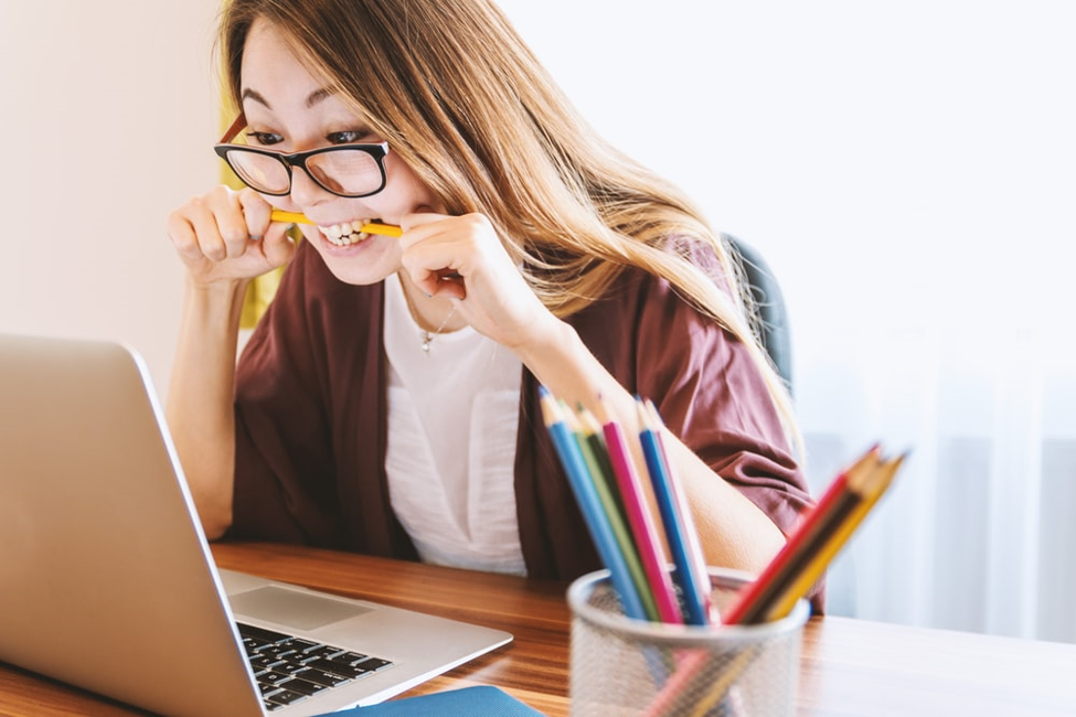 woman biting pencil out of frustration in front of laptop