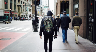 Man in hoodie and backpack walking down a busy city street