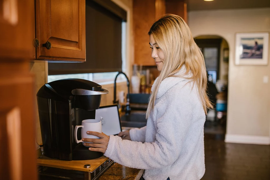 Coffee station in the kitchen - complete with coffee maker and drawer of k-cups. Woman is prepping a cup of coffee