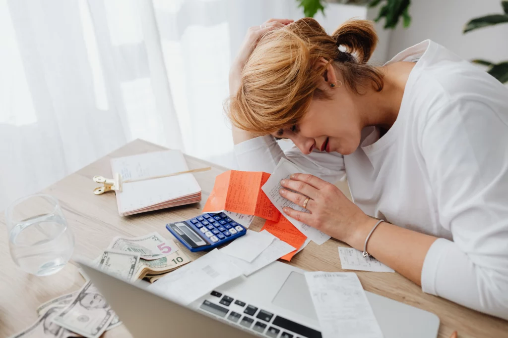 The impact of financial stress. Woman cries while looking at bills, receipts, and her budget.