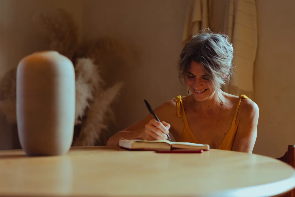 Older woman practices self-care by writing in her journal at the table.