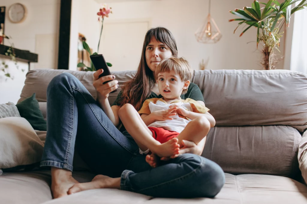 Mother and child relax on cozy couch to watch TV together.