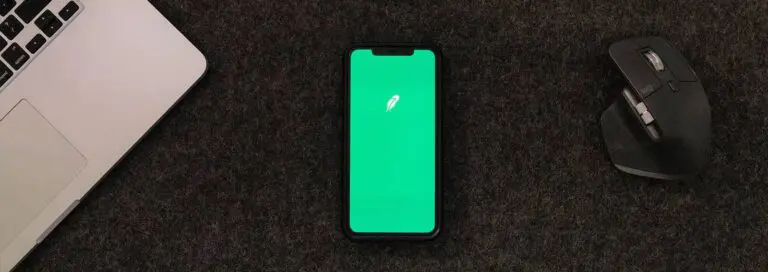 Mobile phone with Robinhood screen pulled up next to laptop and mouse