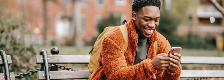 man sitting on bench looking at phone and smiling