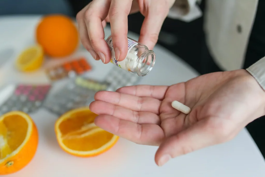 Person placing medication into the palm of their hand. In the background are oranges, and the other medication they take.