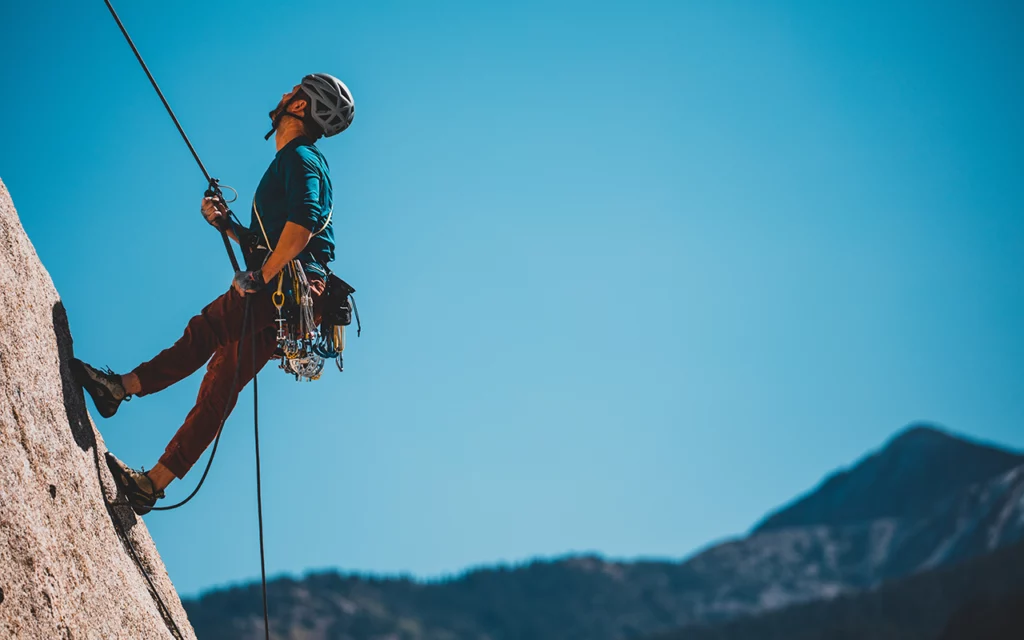 Man with climbing gear rock climbing on the side of a mountain.