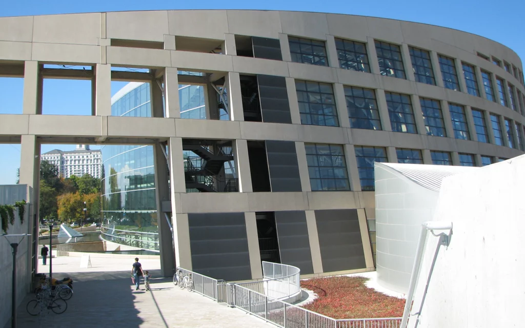 The outside of the large Salt Lake City Public Library. A parent and child walk through the arch. The building is tall and curved, with many windows for natural light.