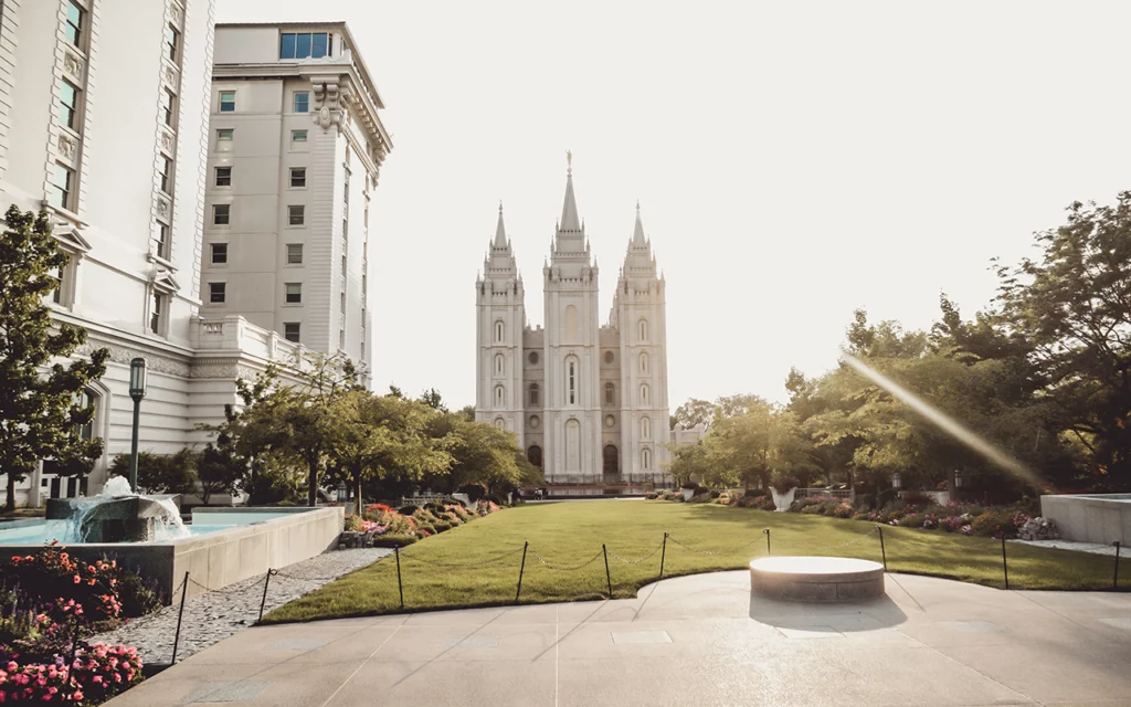 Small grassy section of land has the Salt Lake Temple in the middle of Salt Lake City. You can see large modern buildings next to it.