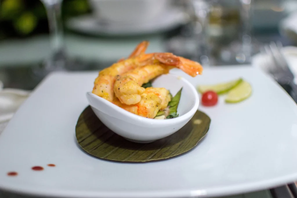 Image shows a bowl with two shrimps in it, placed on a platter with garnishing.